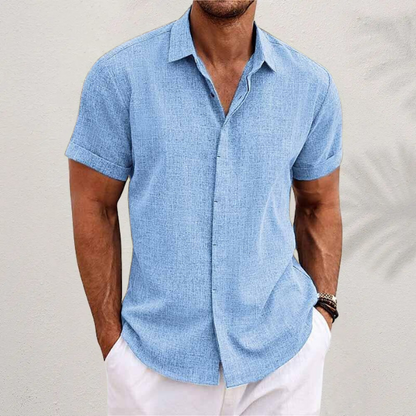 Light blue textured short-sleeved shirt with cuffed sleeves, worn by a model with white trousers against a pale wall. 8