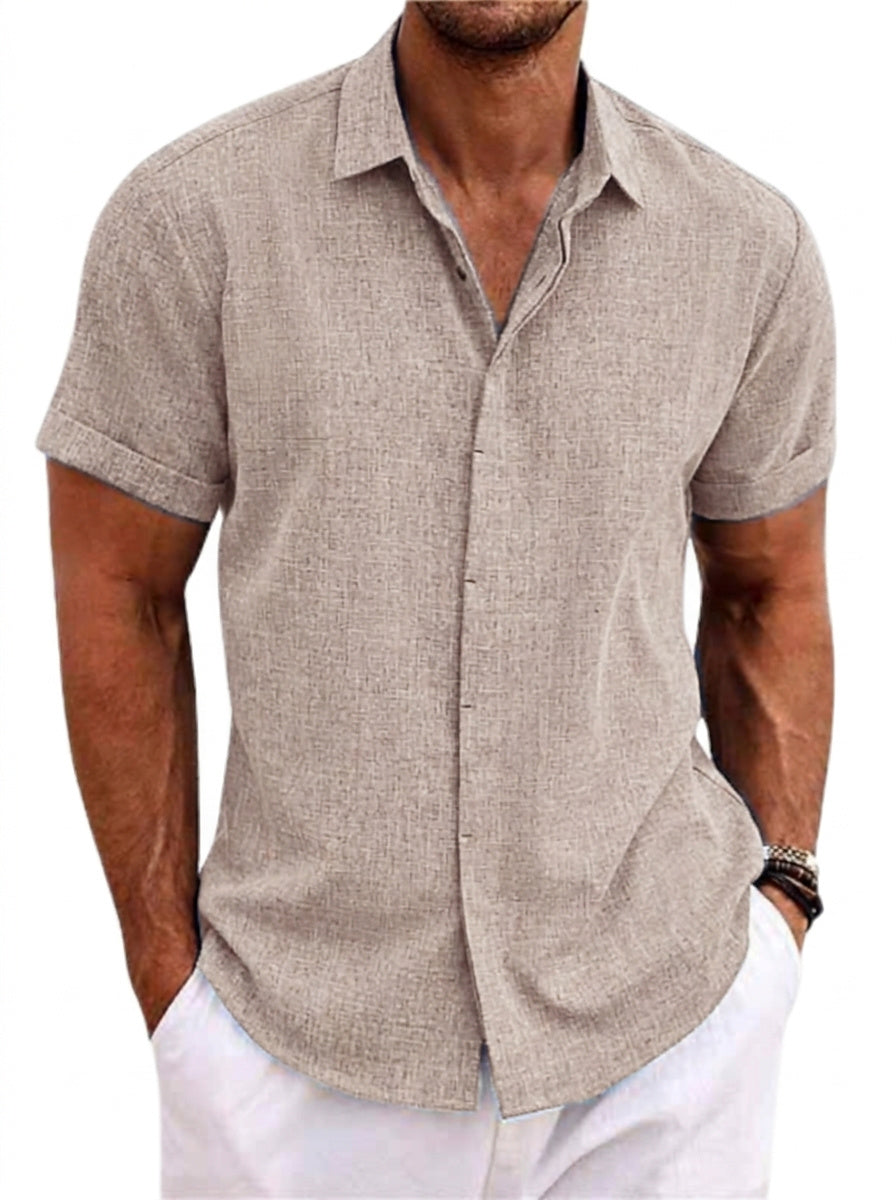 Close-up of a taupe textured short-sleeved shirt with turned-up cuffs, worn by a model with hands in white trouser pockets. 1