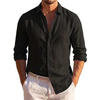 Black linen shirt with a button placket and rolled sleeves, worn open at the neck with cream trousers against a white background. 3