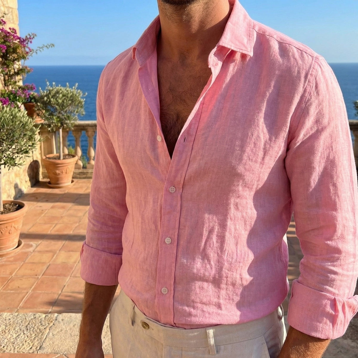 Pink linen shirt with cuffs turned back, worn open at the collar on a terrace with potted olive trees and the sea beyond. 8