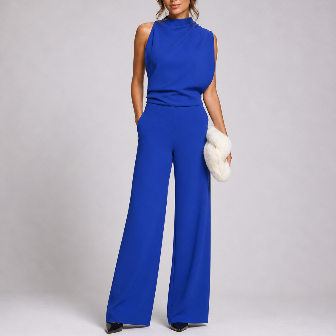 Model wears the jumpsuit in royal blue with a draped neckline and black shoes, carrying a fluffy cream clutch 6