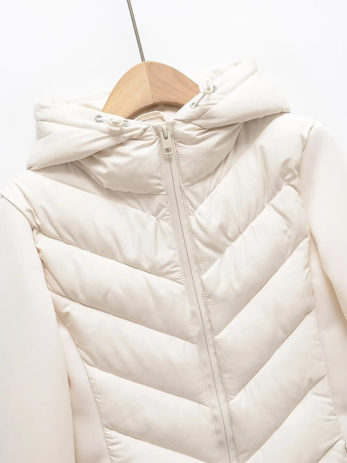 Close-up of the cream jacket's quilted hood, drawstring toggles and front zip, hanging on a wooden hanger. 3