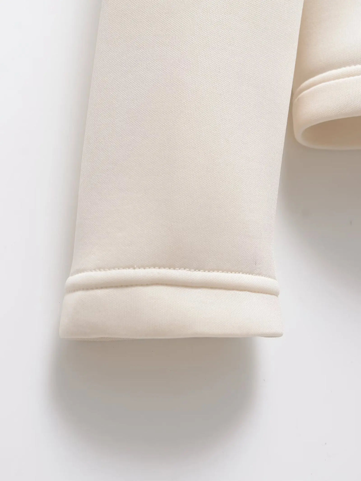 Close-up of a cream sleeve cuff, showing the neat double-stitched hem and soft fabric texture. 5