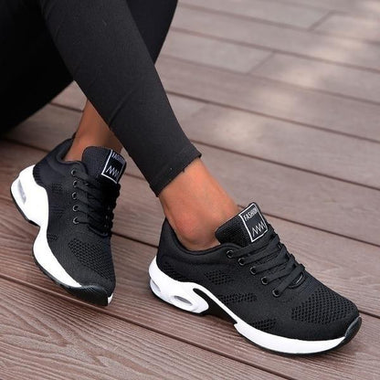 All-black breathable mesh trainers with a white air-cushion sole, worn with black leggings on a wooden deck. 3