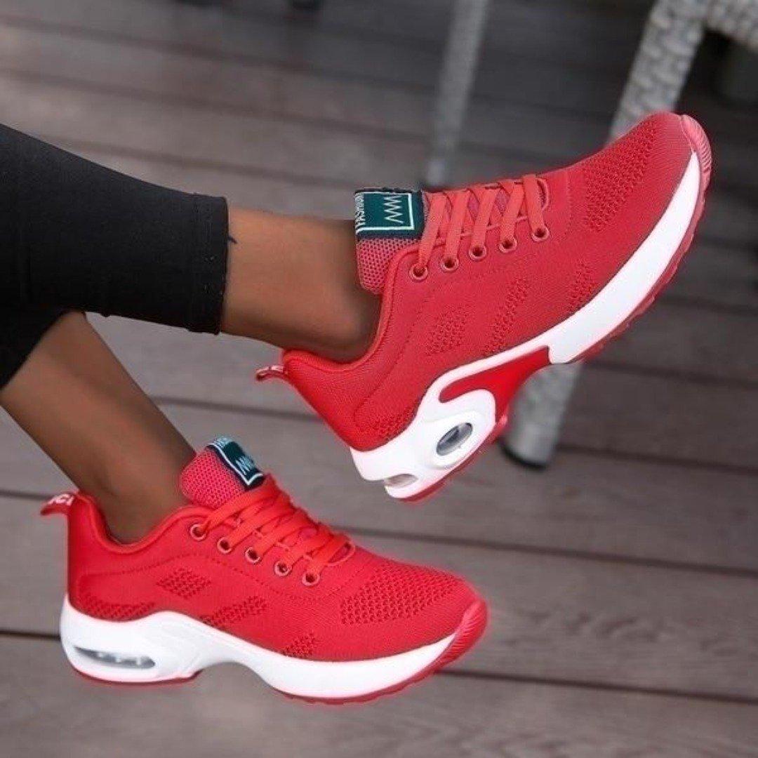 Bright red mesh trainers with a white air-cushion sole and matching red laces, shown worn with one foot raised. 7