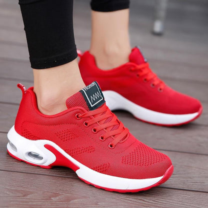 Close-up of a red mesh trainer with white cushioned sole and air window, worn by a model on wooden boards. 5