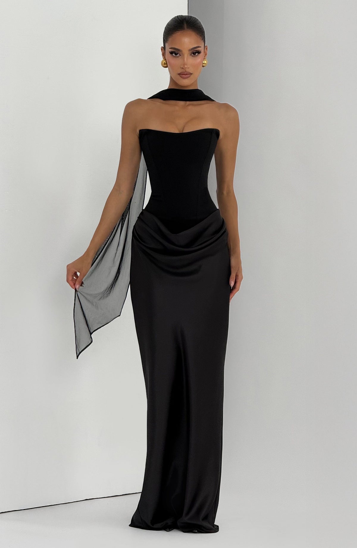 Black corset dress with a sheer scarf draped around the neck and held out at one side 27
