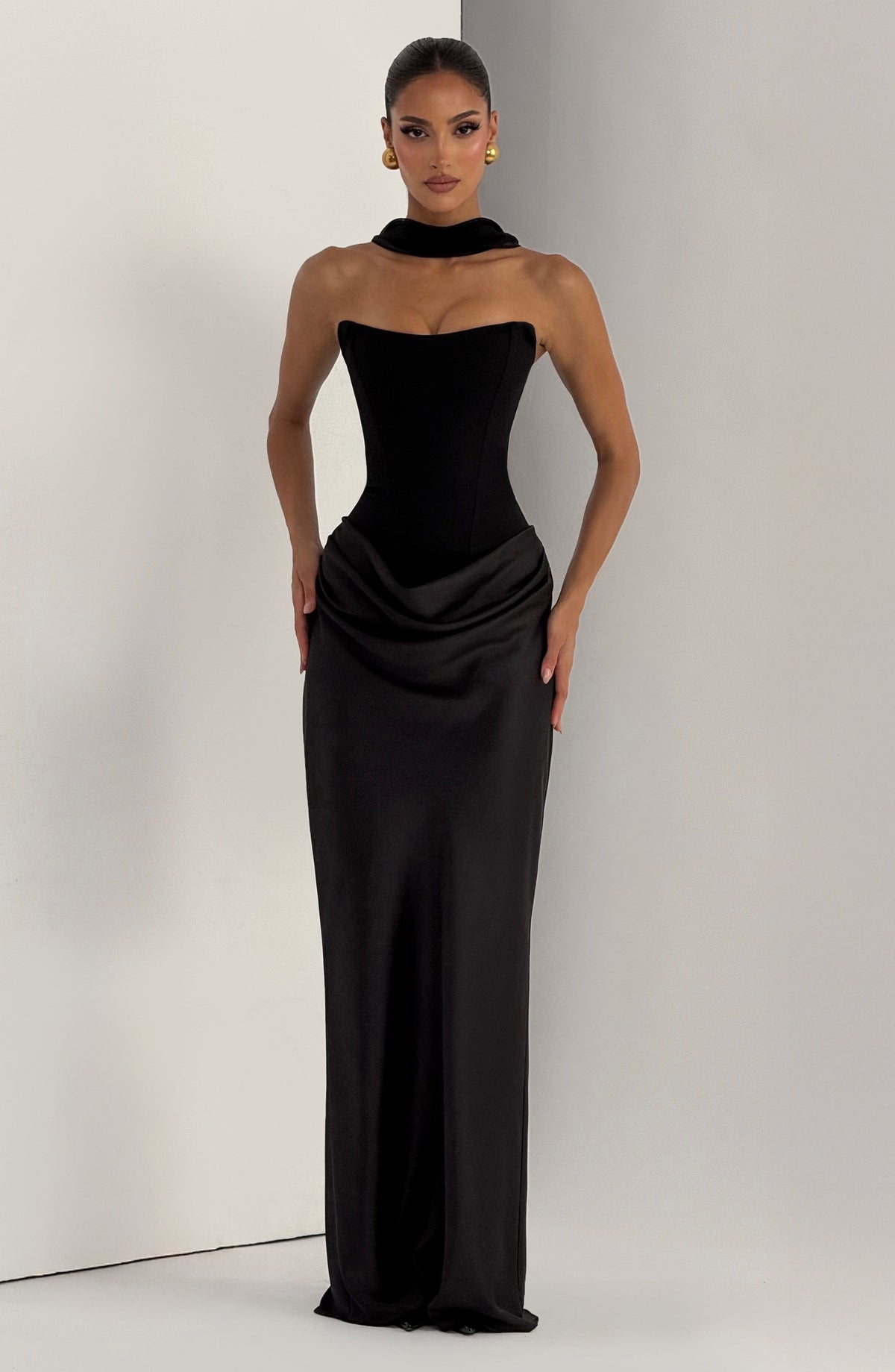 Black strapless dress styled with a fabric collar choker, model standing in a studio corner 26