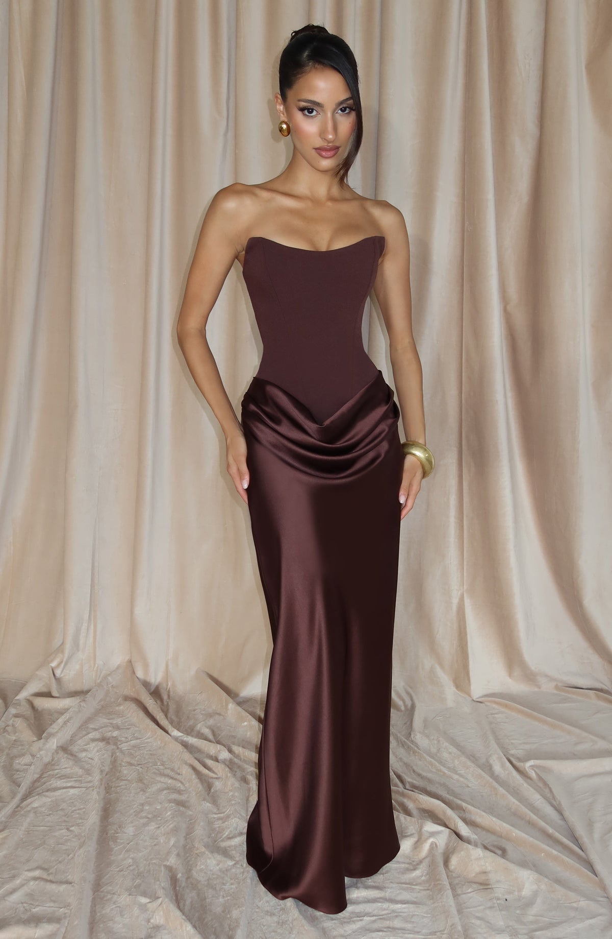Model poses with one hand on hip in the brown maxi dress against cream curtains 8