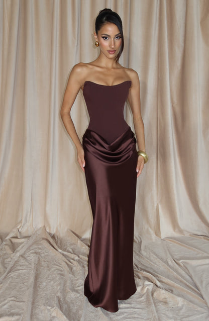Model poses with one hand on hip in the brown maxi dress against cream curtains 8