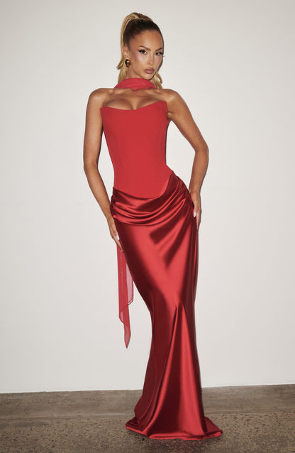 Blonde model in the red corset dress and scarf posing against a plain white wall 14
