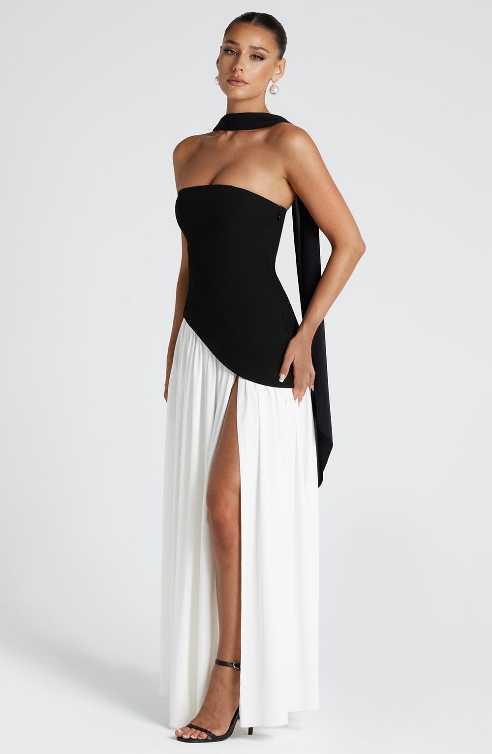Model in the black and white version of the dress, with a black strapless bodice, white gathered skirt and thigh slit. 9