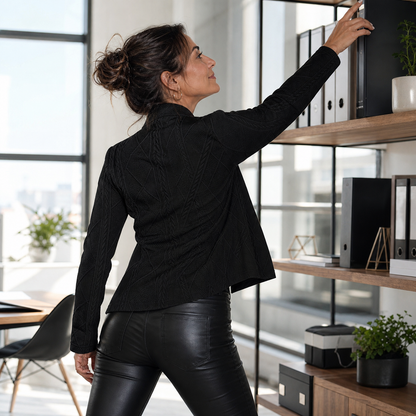 Back view of the black textured blazer, worn with leather-look trousers while reaching for an office shelf 13