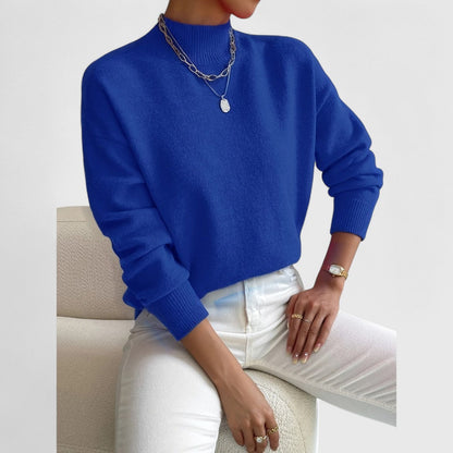 Vivid royal blue jumper on a seated model with white jeans, silver chain necklaces and ribbed cuffs. 11