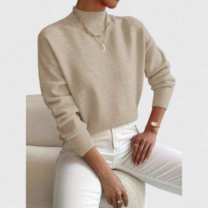 Beige jumper on a seated model with white jeans and gold chain necklaces, showing the relaxed fit and ribbed cuffs. 7