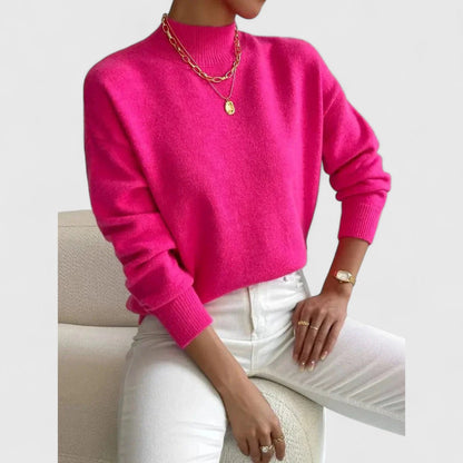 Bright fuchsia pink jumper on a seated model, styled with white jeans, gold layered necklaces and a gold watch. 9