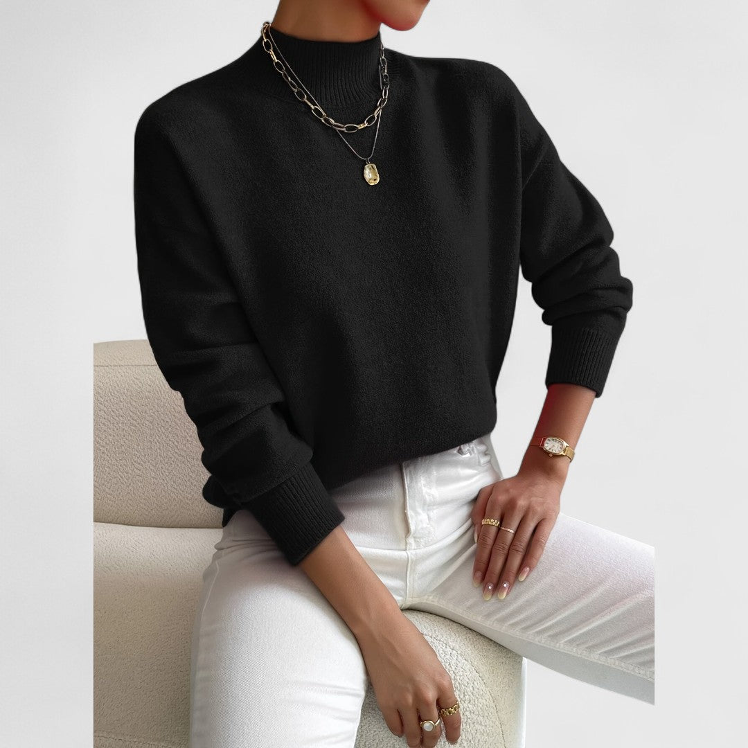 Black jumper worn by a seated model with white jeans, gold necklaces, a gold watch and rings. 8