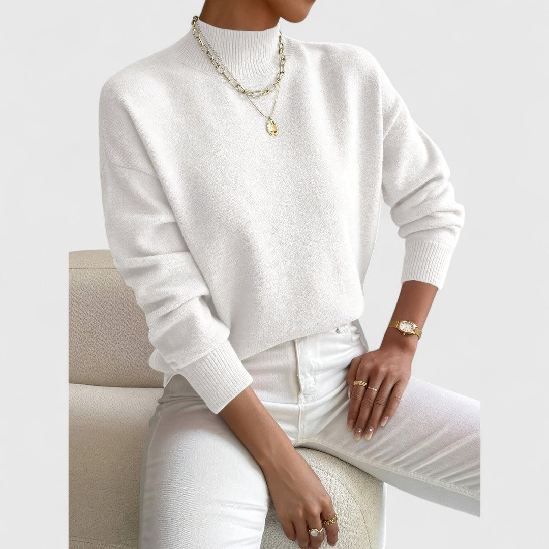 Cream white jumper worn by a seated model with white jeans, gold layered necklaces and a gold-strap watch. 4