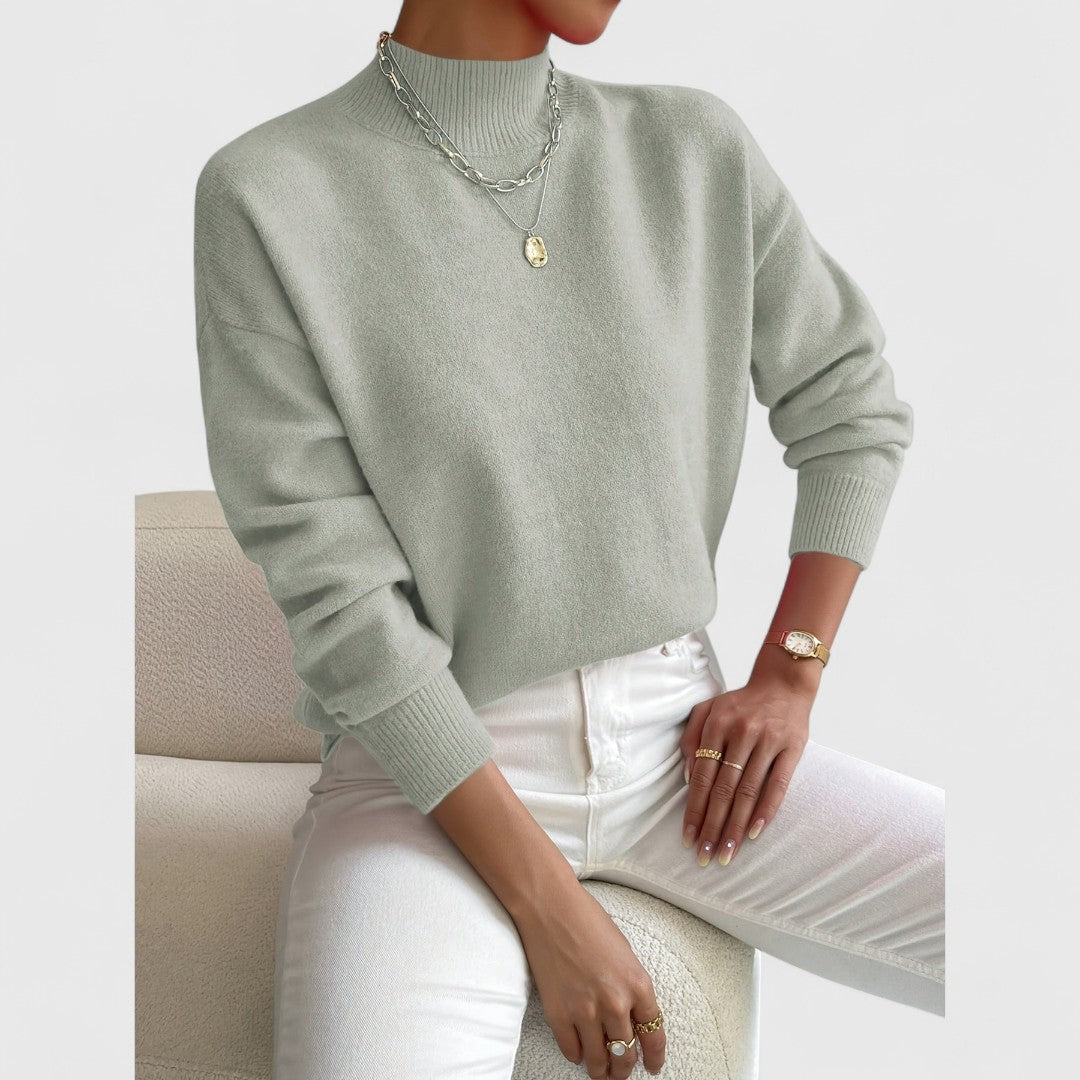 Sage green jumper shown in a slightly closer crop on a seated model, with a loose drop-shoulder fit and ribbed hem. 3