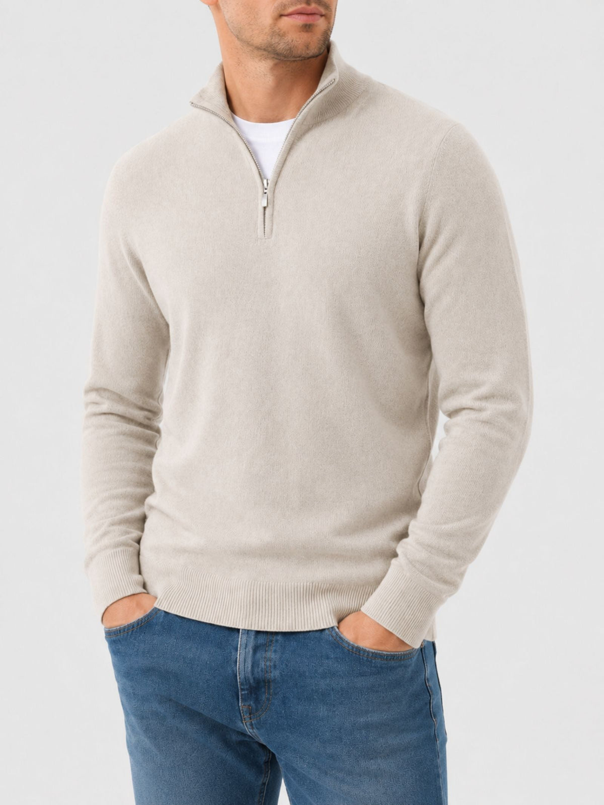 Model in a cream quarter-zip jumper with stand collar, hands in the pockets of blue jeans, shown from the front. 1