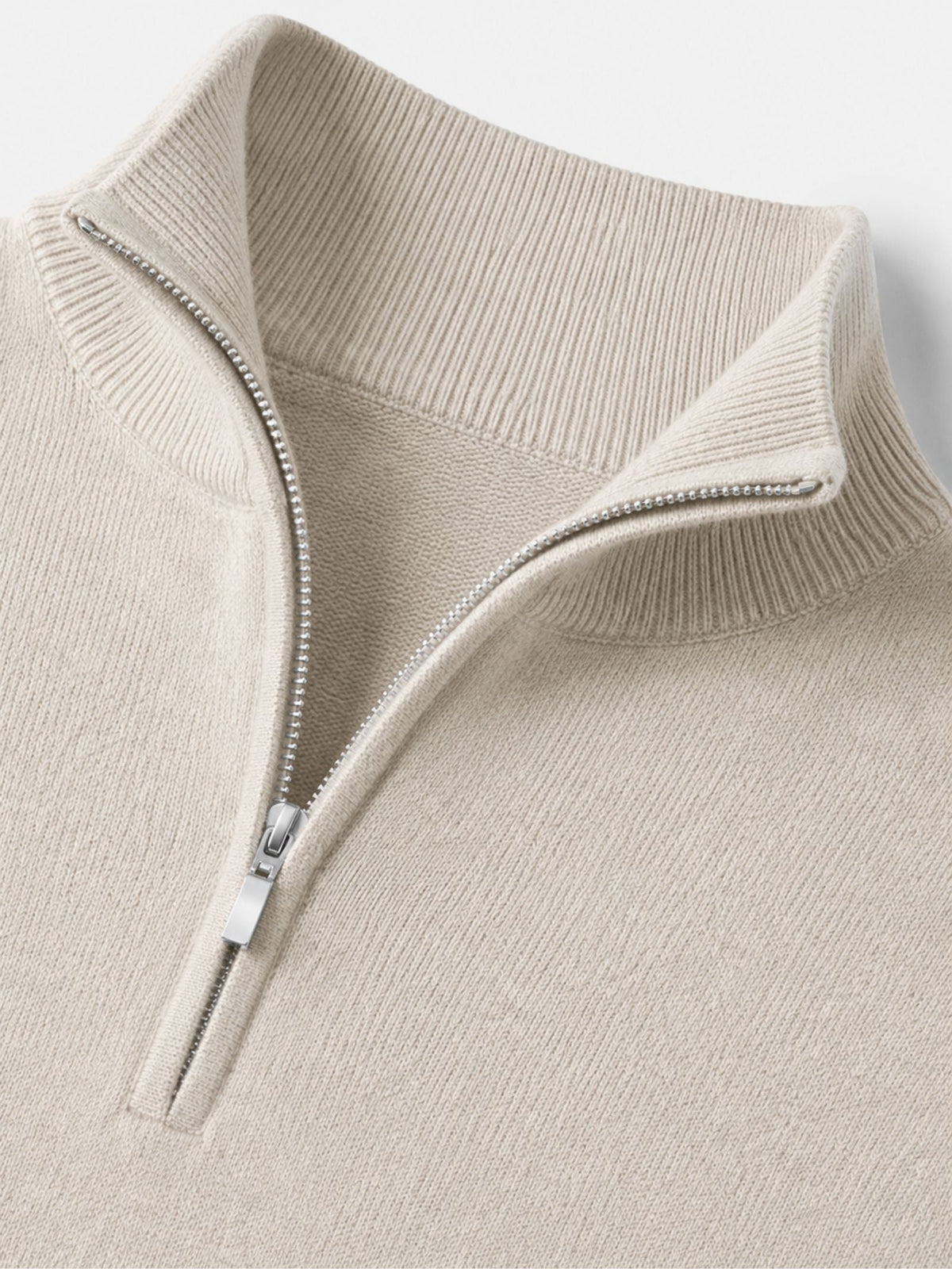 Close-up detail of the cream jumper's ribbed stand collar and silver metal half zip with pull tab. 14