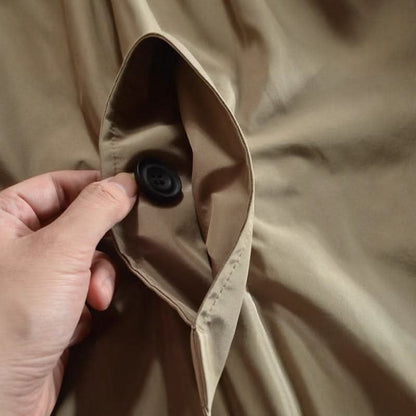 Close-up of a hand holding open a beige coat's inner pocket, showing a black button 8