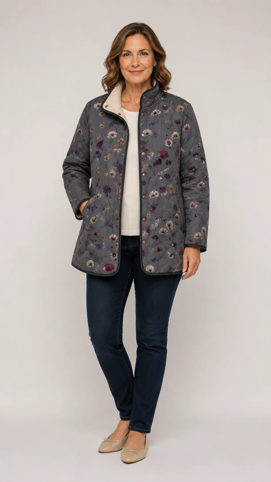 Woman wearing the grey floral quilted jacket open over a cream top, dark jeans and beige flats, full-length front view. 1