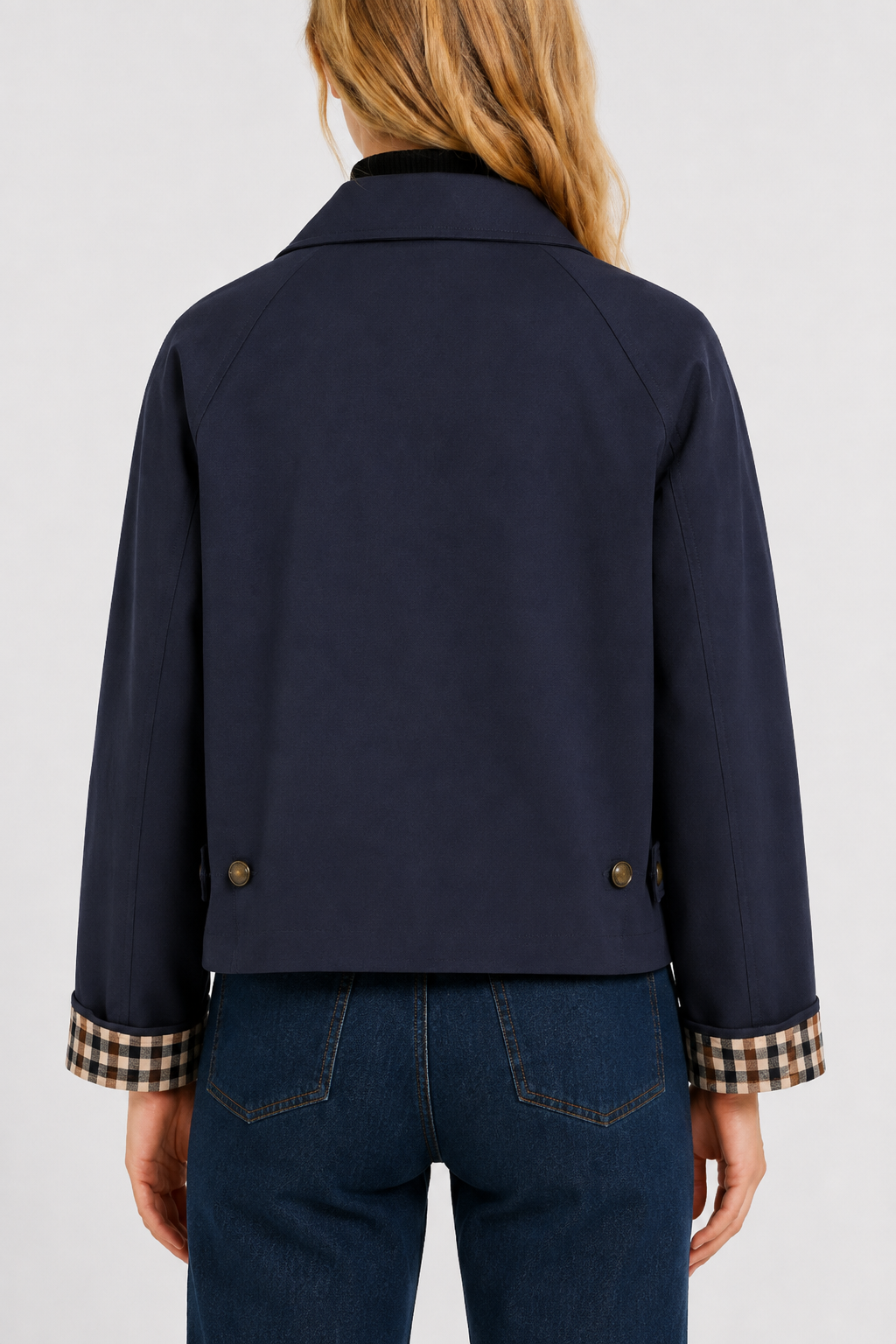 Back view of the navy jacket with raglan sleeves, two buttoned tabs at the hem and gingham cuff lining. 15