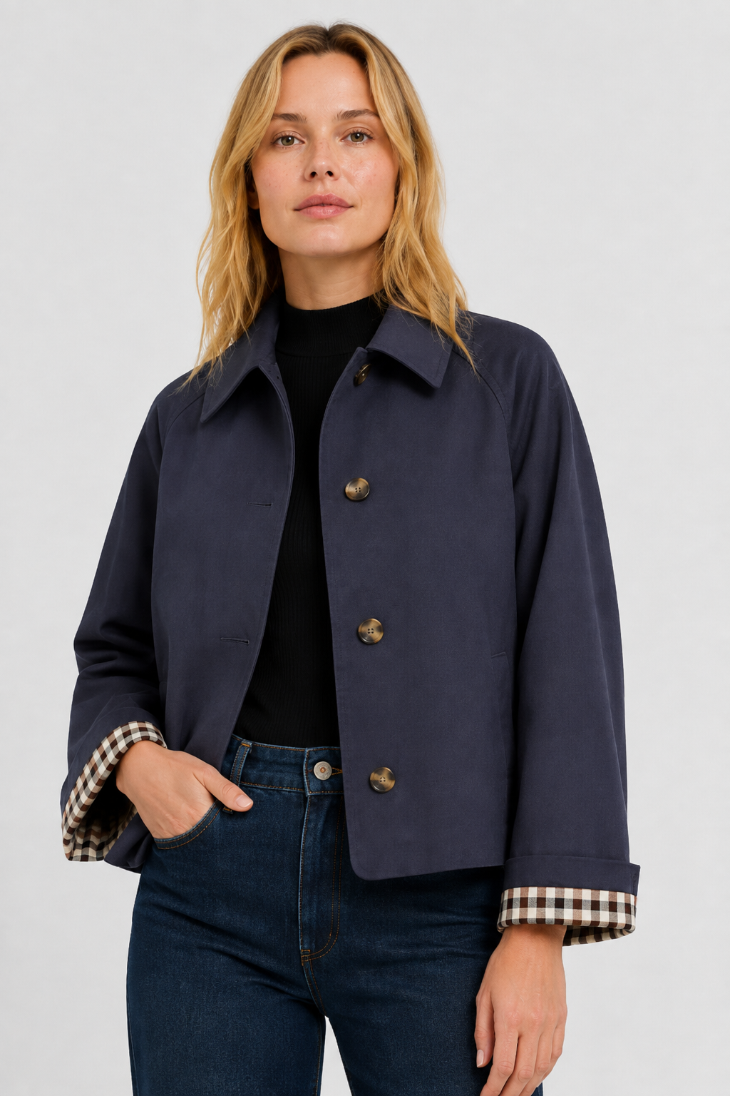 Model wears the navy jacket open over a black top and jeans, one hand in pocket, gingham cuff lining visible. 13