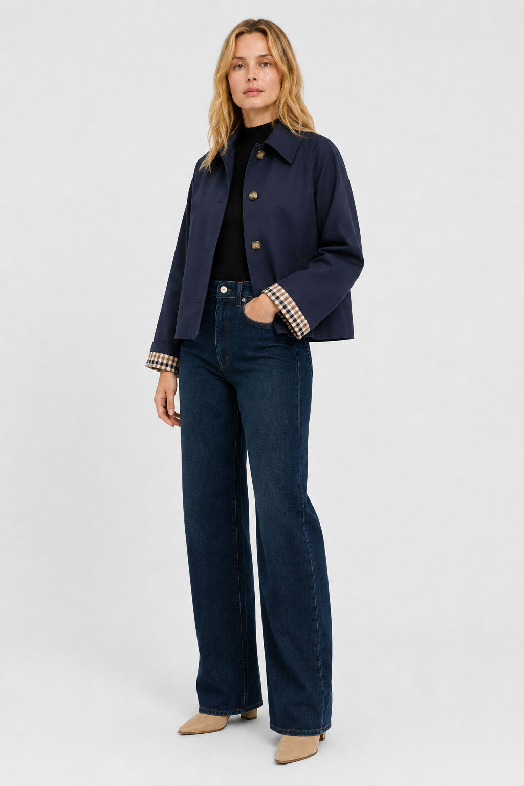 Full-length view of the navy jacket worn with a black top, dark wide-leg jeans and beige boots, hand in pocket. 16
