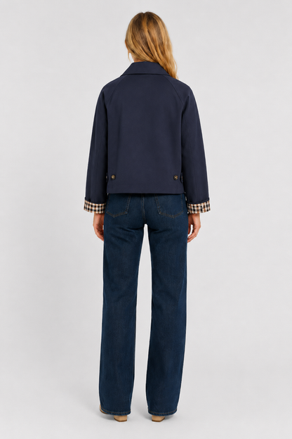 Full-length back view of the navy jacket, cropped length, with buttoned back tabs and gingham cuffs, worn with dark jeans. 17