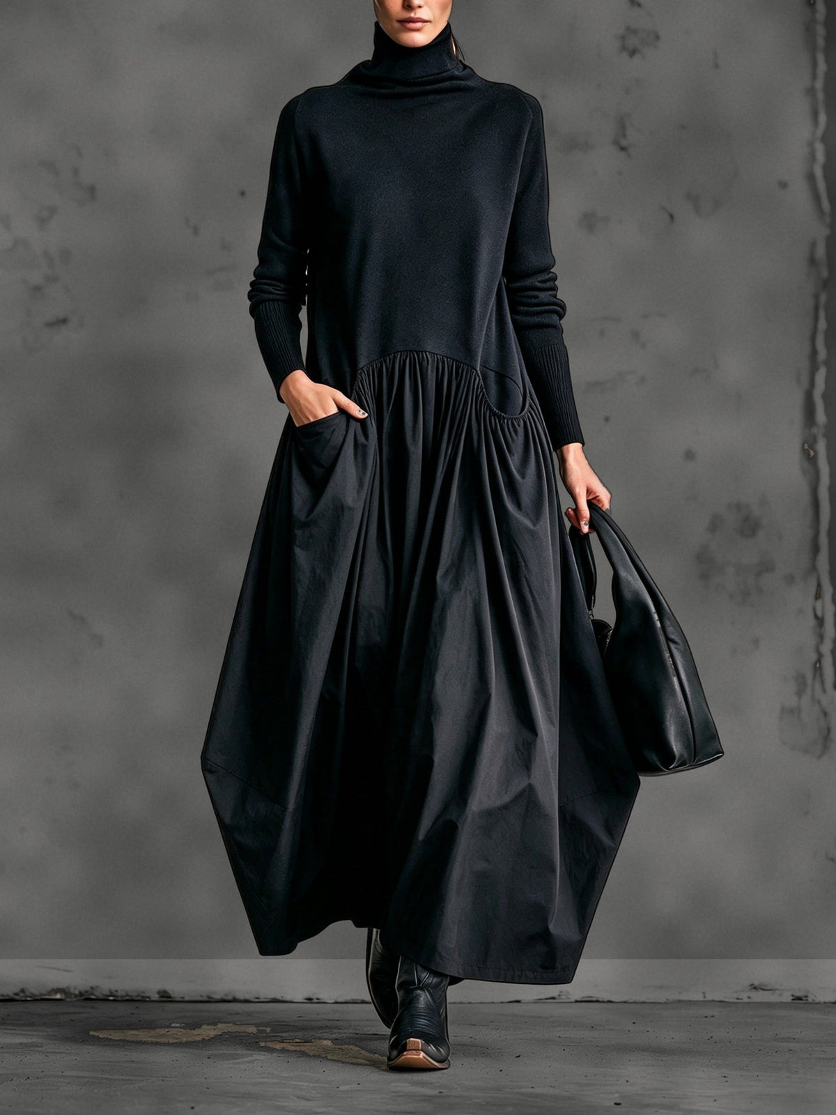Model wearing the black dress from the front, one hand in a pocket, holding a leather bag 1