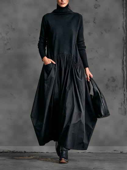 Model wearing the black dress from the front, one hand in a pocket, holding a leather bag 1