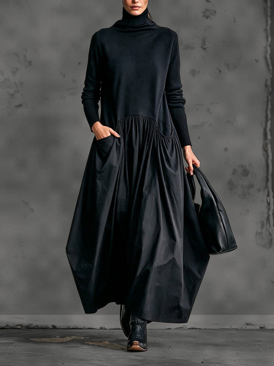 Model wearing the black dress from the front, one hand in a pocket, holding a leather bag 1