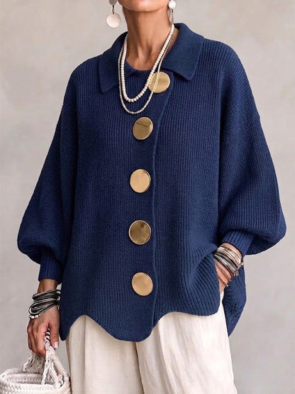 Model wearing the navy ribbed cardigan from the front, with large gold buttons, collar, balloon sleeves and scalloped hem, styled with cream trousers. 1