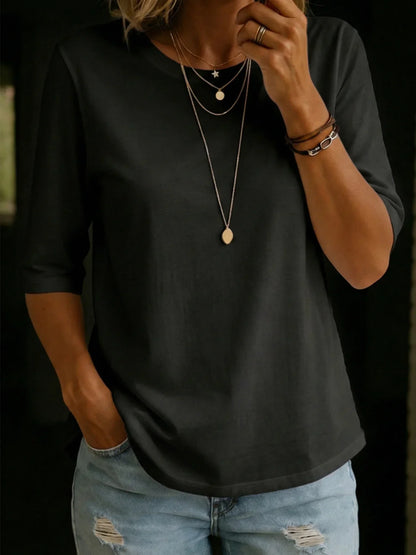 Woman wearing the black half-sleeve crew-neck tee with layered gold necklaces, stacked bracelets and ripped light-wash jeans. 4