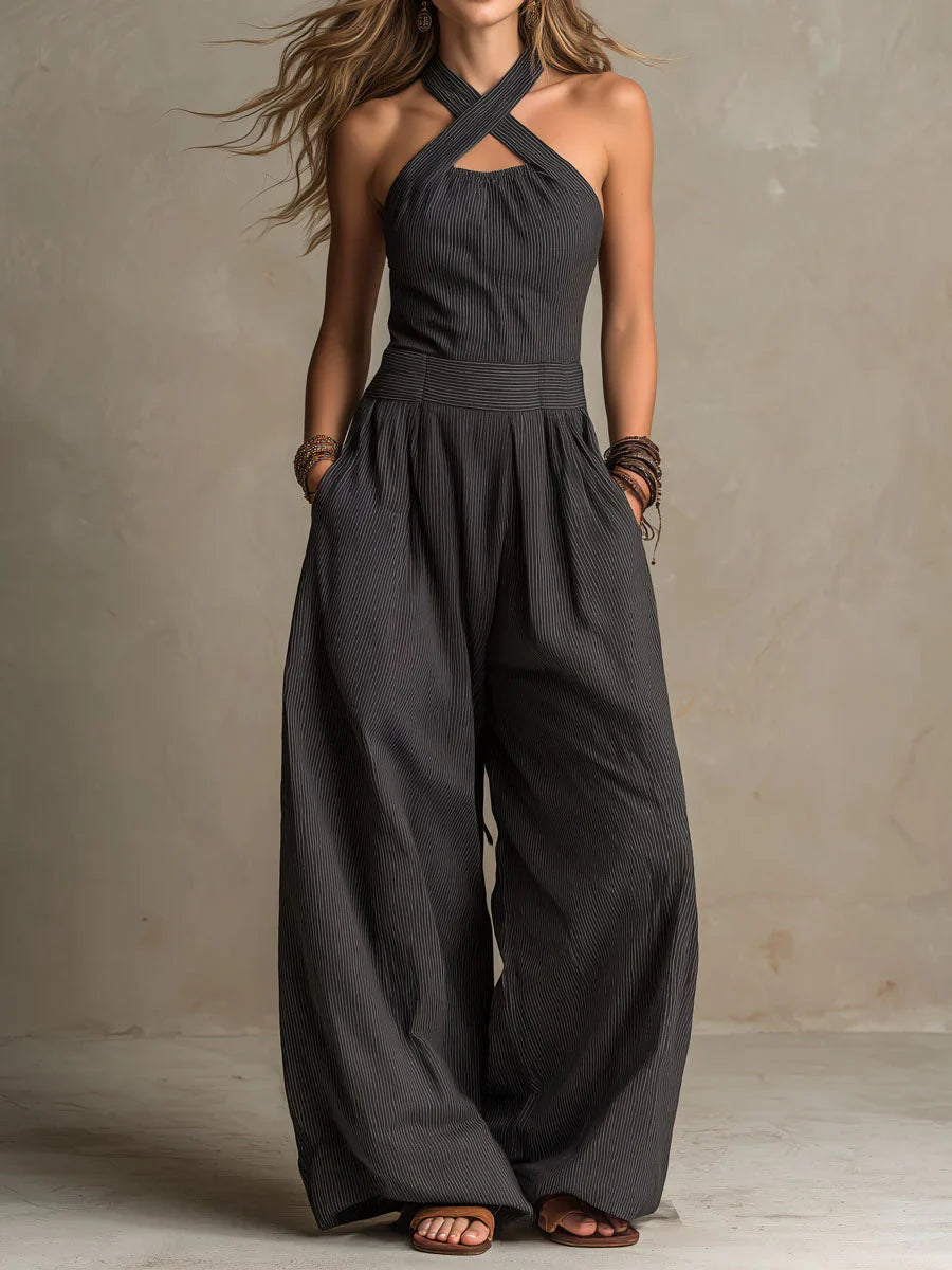 Model wearing the halterneck jumpsuit in dark charcoal pinstripe, hands in pockets, with wide legs 1