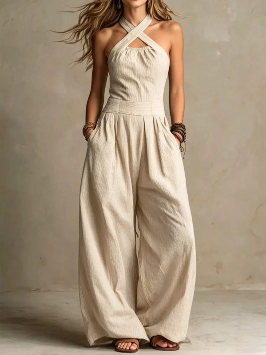 Model wearing the crossover halter jumpsuit in cream, with pleated wide legs and brown sandals 2