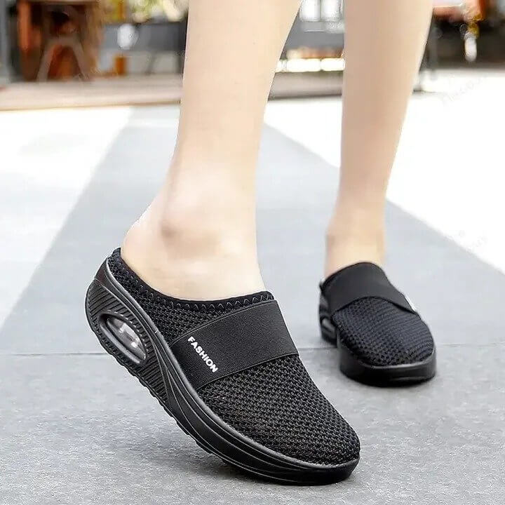 Black mesh slip-on mules with air cushion heel, worn by a model walking outdoors on pavement 3