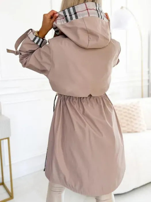 Back view of the beige hooded jacket on a model with the hood held up, showing the gathered waist and checked hood lining. 3