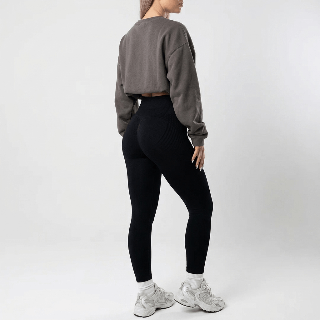 Back view of plain black high-waisted leggings styled with an oversized grey sweatshirt and white socks with silver trainers. 25
