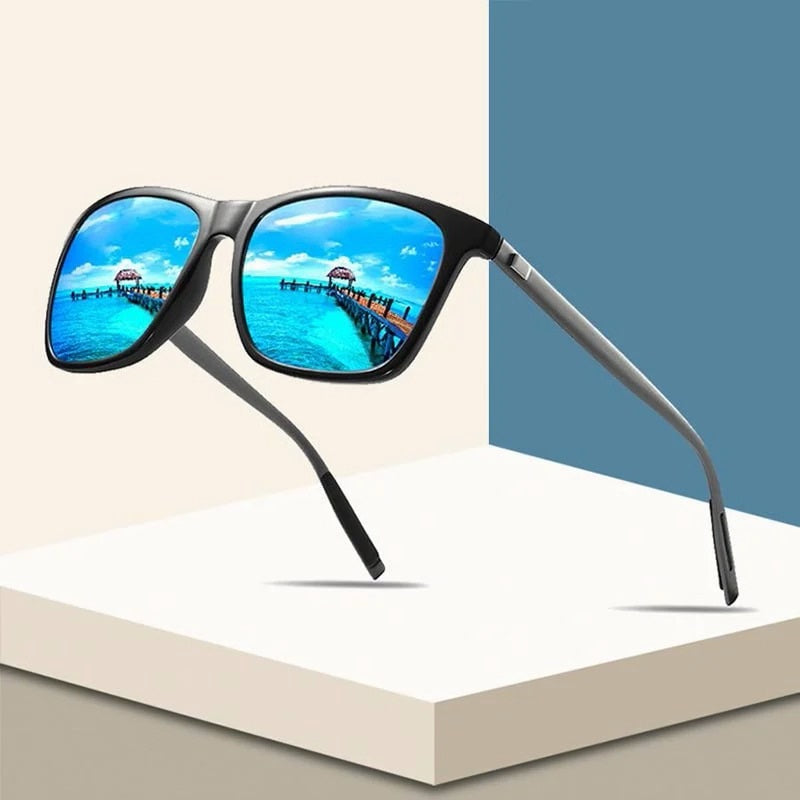Black square-framed sunglasses with blue mirrored lenses reflecting a tropical pier, displayed on pale geometric blocks 1