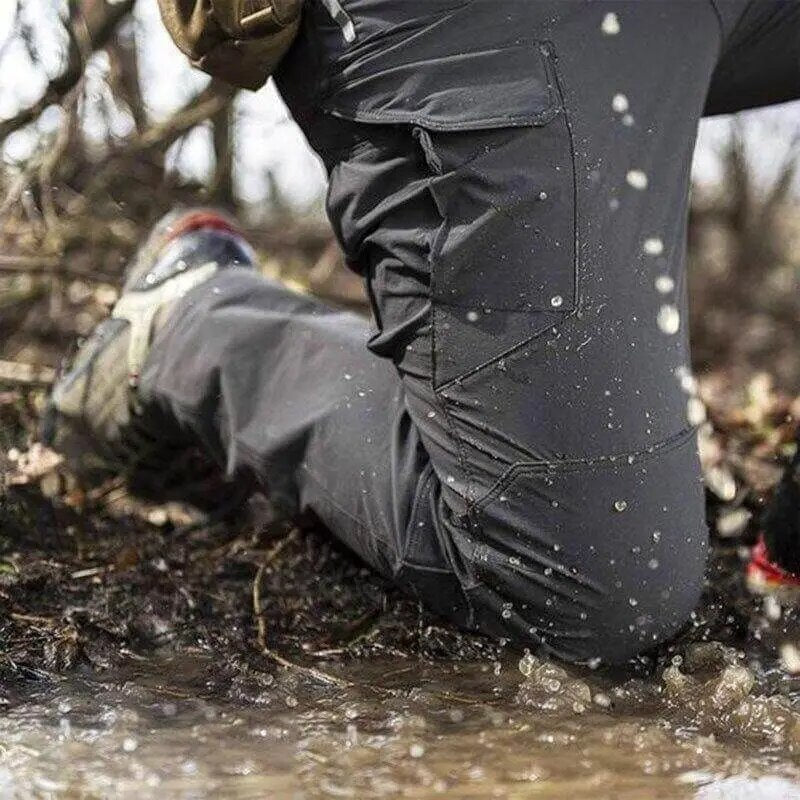Close-up of grey trousers on a kneeling wearer in a muddy puddle, with water splashing and beading on the fabric. 3