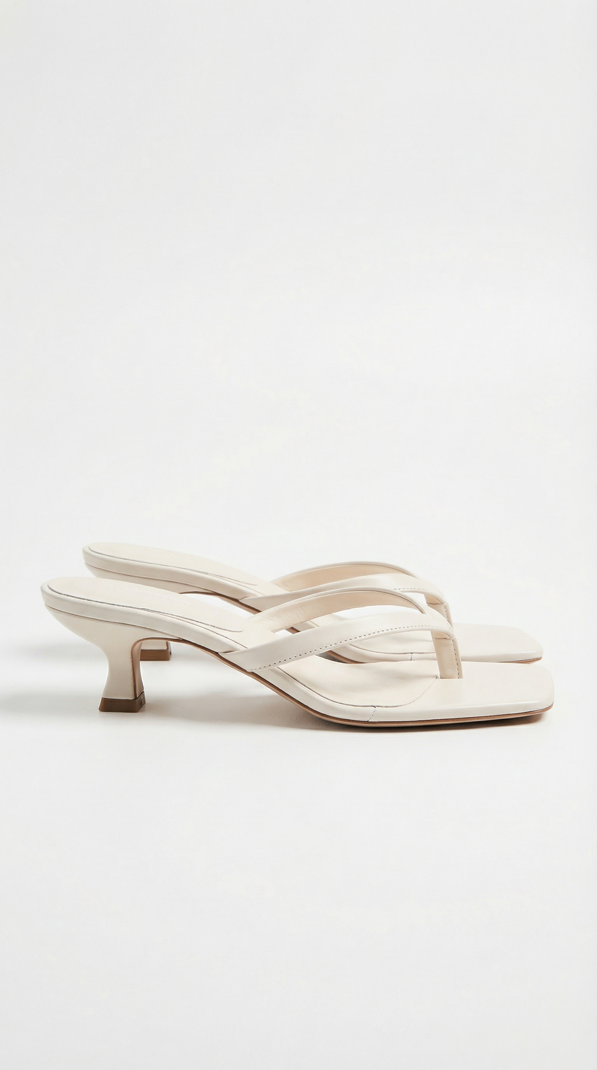 Pair of cream kitten-heel thong sandals with square toes and slim straps, shown from the side on white. 10