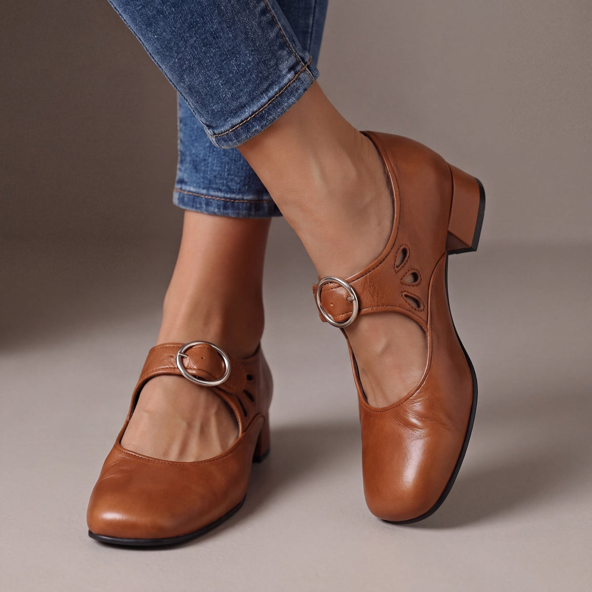 Tan brown leather block-heel pumps worn with cropped jeans, showing a round silver buckle strap and teardrop cut-outs on the side. 3