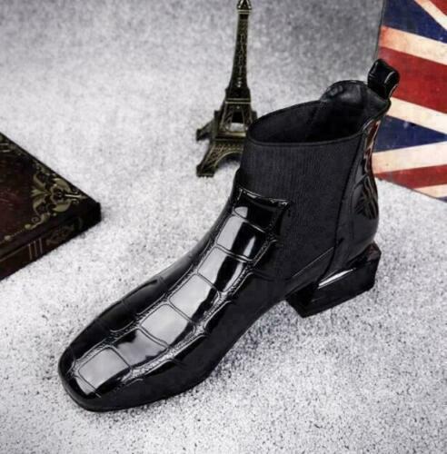 Black croc-effect Chelsea-style boot seen from above at an angle, beside a small tower ornament and flag 5
