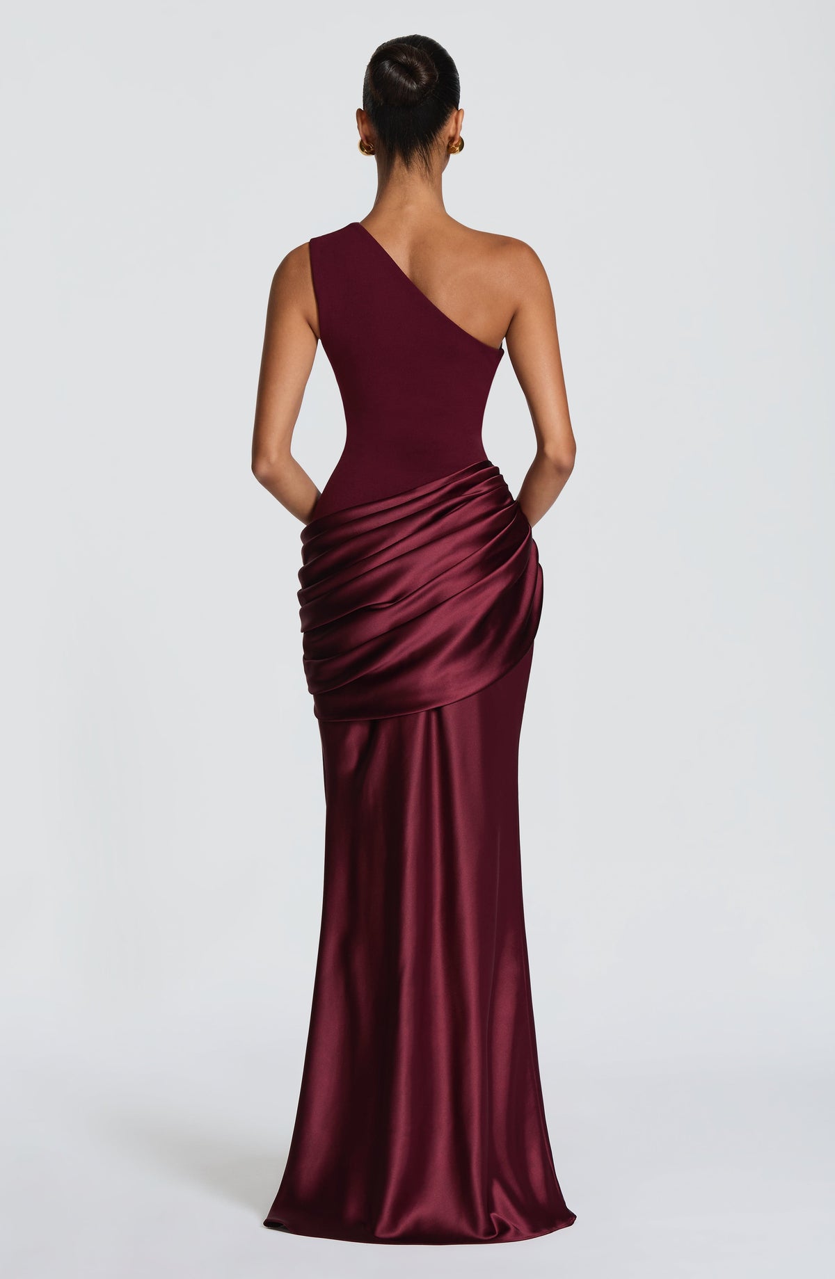 Model in the burgundy one-shoulder dress posing against a plain wall, one arm raised behind her head. 32