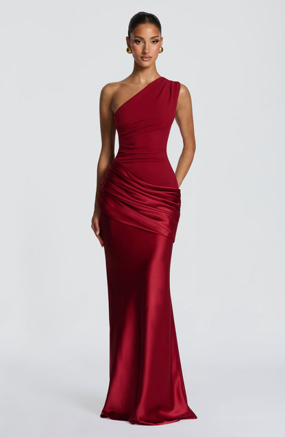 Model wearing the one-shoulder maxi dress in deep red, front view, with pleated crepe bodice and draped satin hip panel. 21
