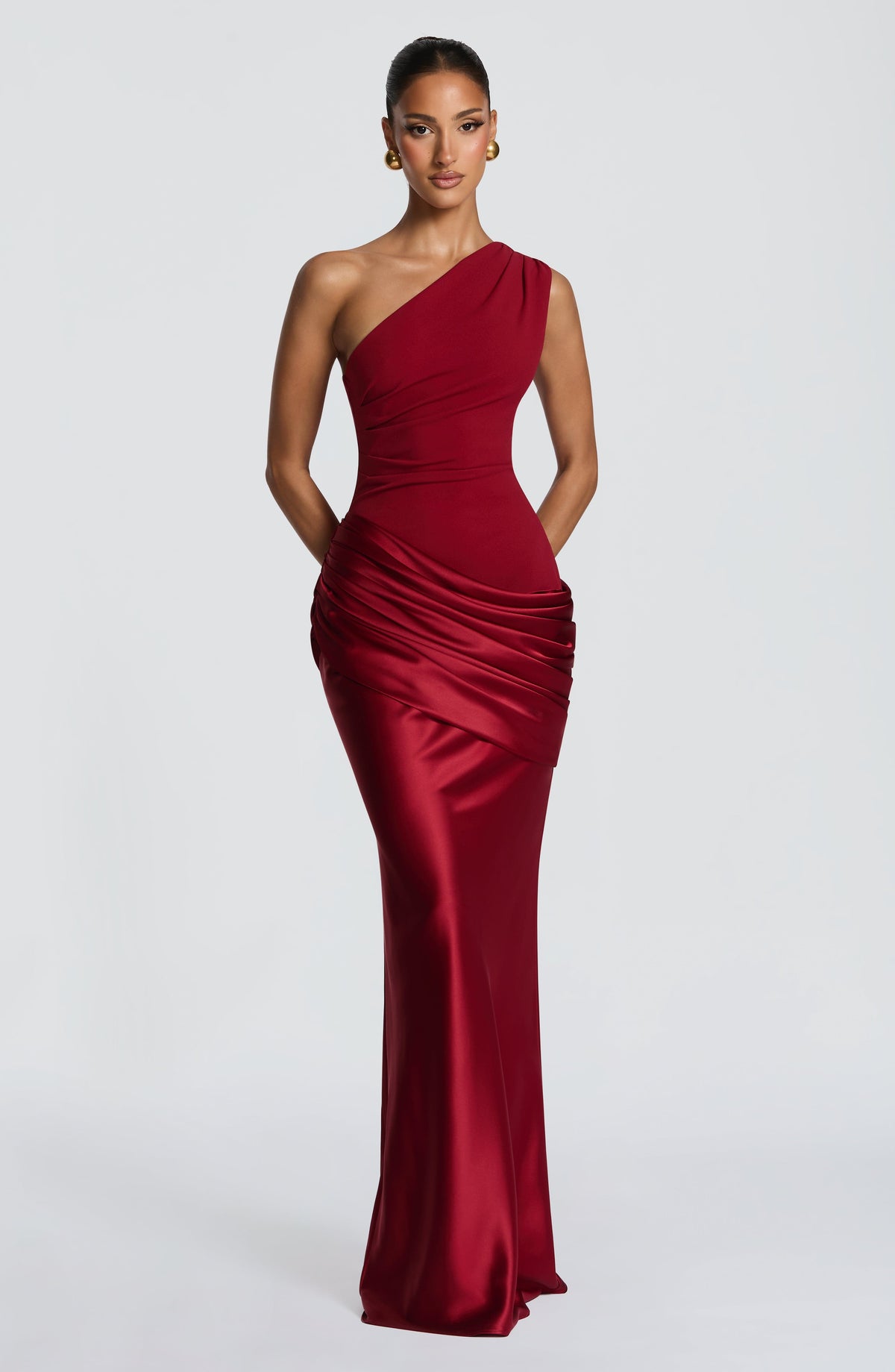 Red one-shoulder satin maxi dress worn with hands tucked behind the back, showing the ruched hip drape and fitted silhouette. 20