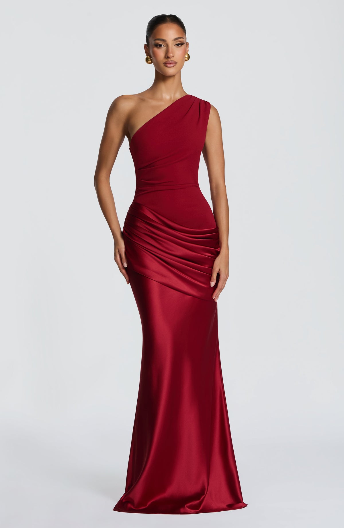 Front view of the deep red one-shoulder maxi dress with ruched satin hip drape and gold ball earrings. 15